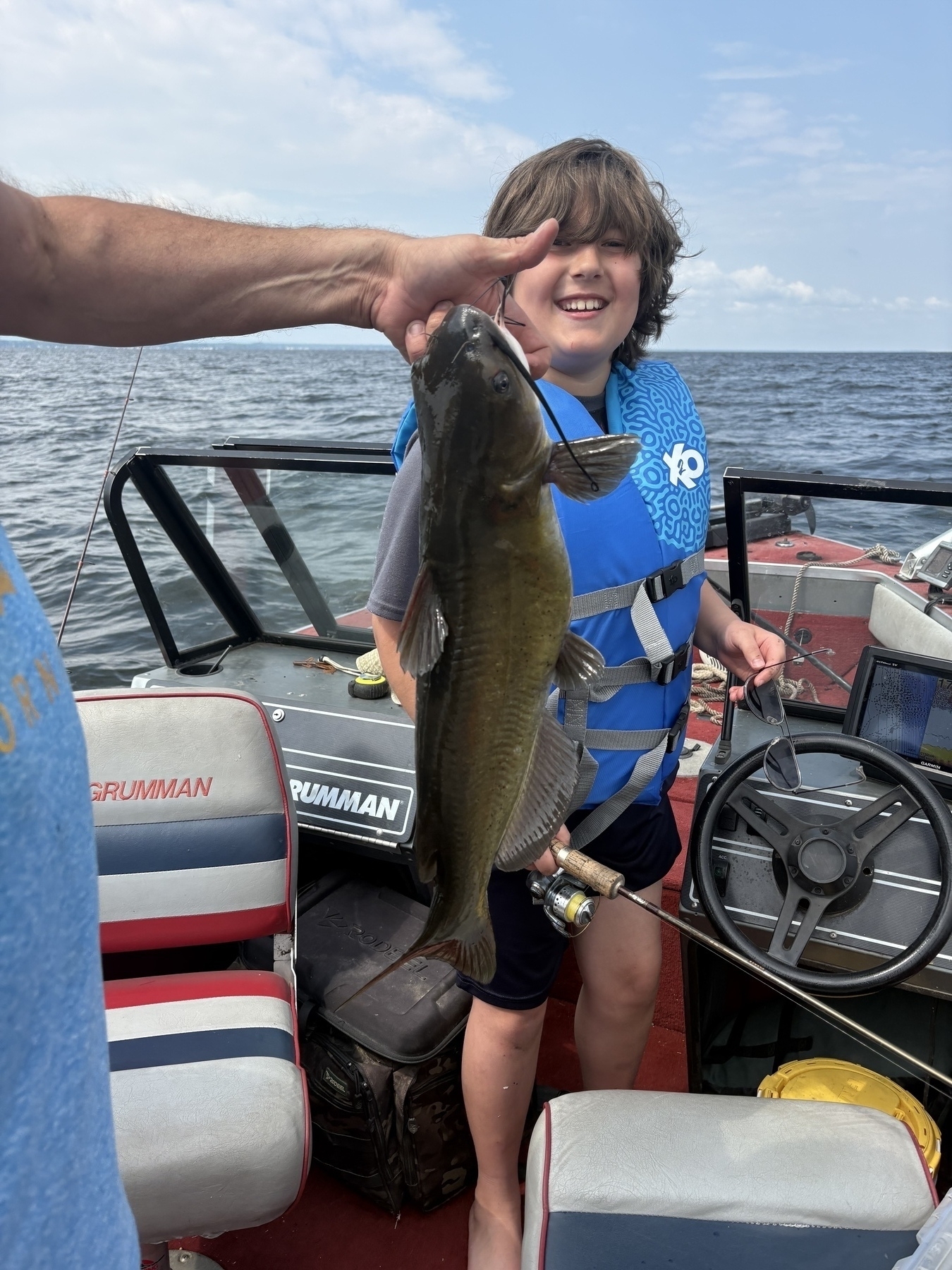 My brother in law holds up a fish while my oldest son wearing a life jacket smiles on a boat.